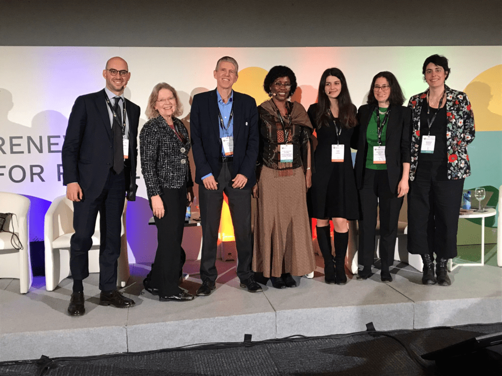 Panellists standing on stage with conference poster as a backdrop
