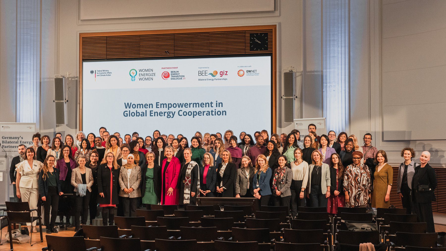 BETD 2023 Women Energize Women Event participants stand together on stage with the event poster as a backdrop
