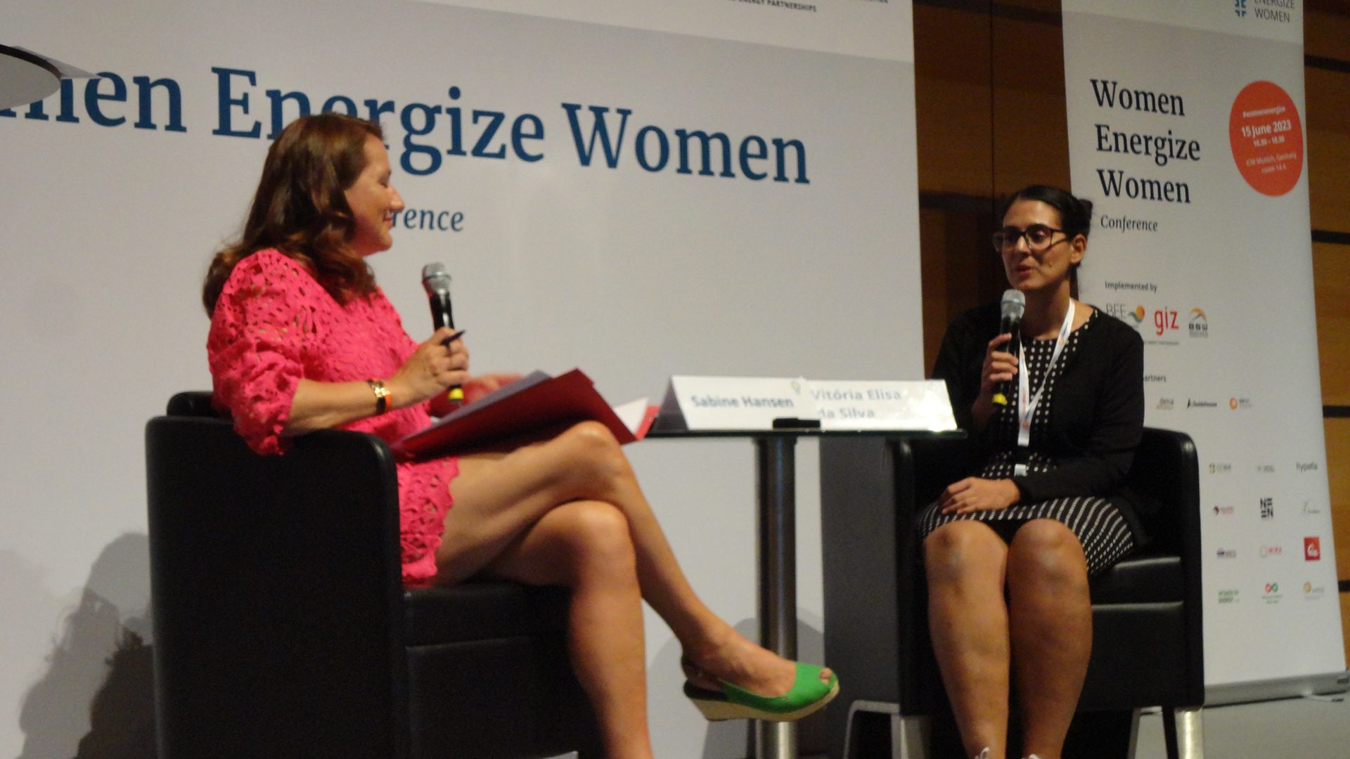 Two women on stage facing each other. One is carrying a mic in her hand